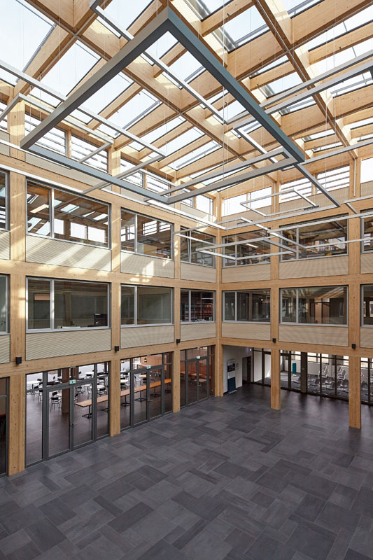 Das Atrium mit seinem Brettsperrholz Dachtragwerk schließt an die Kantine und Schulungsbereich im EG an. (Quelle: ZRS Architekten)